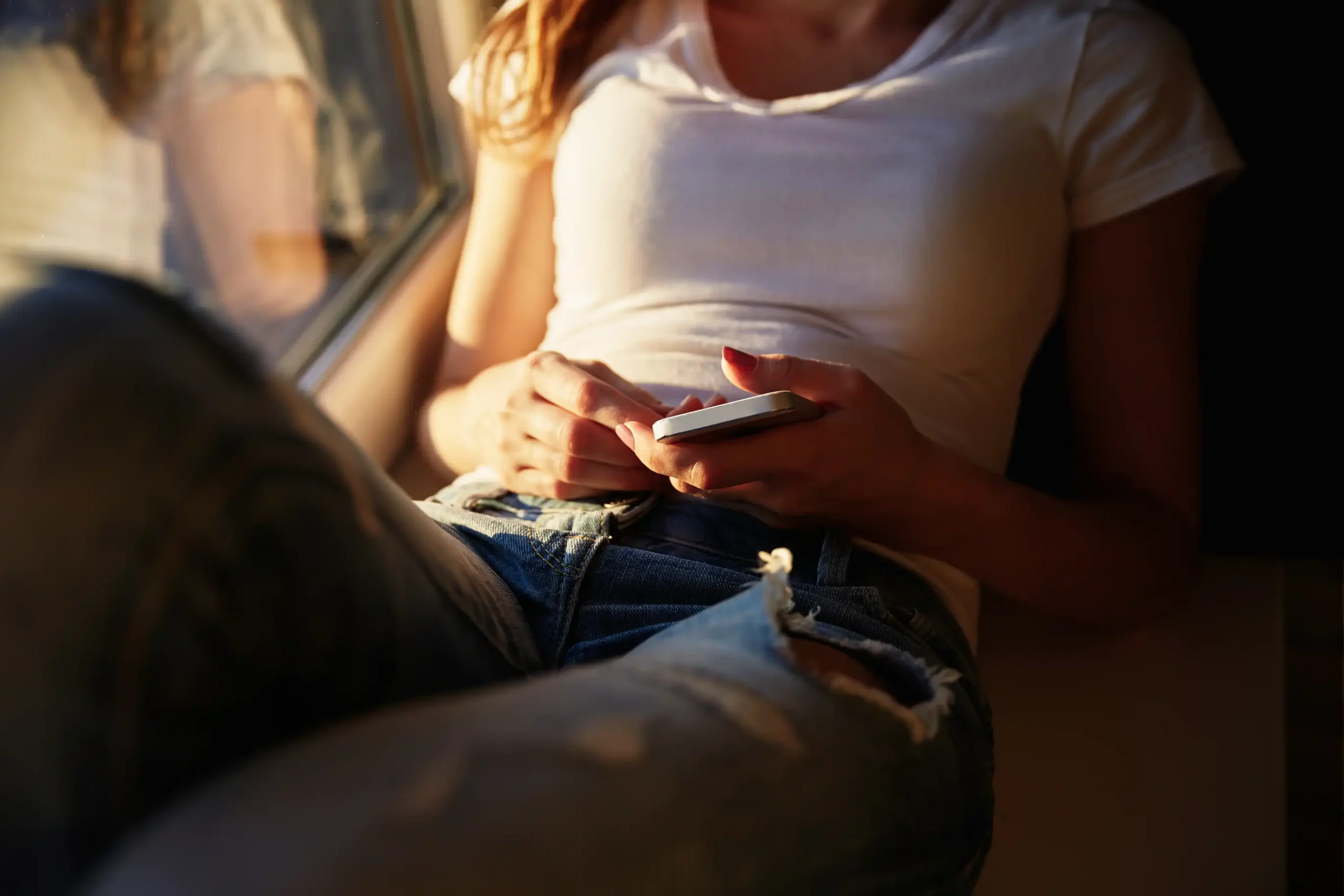 Joven mujer trans revisando su cuenta de OnlyFans en el móvil, relajada en casa con luz natural