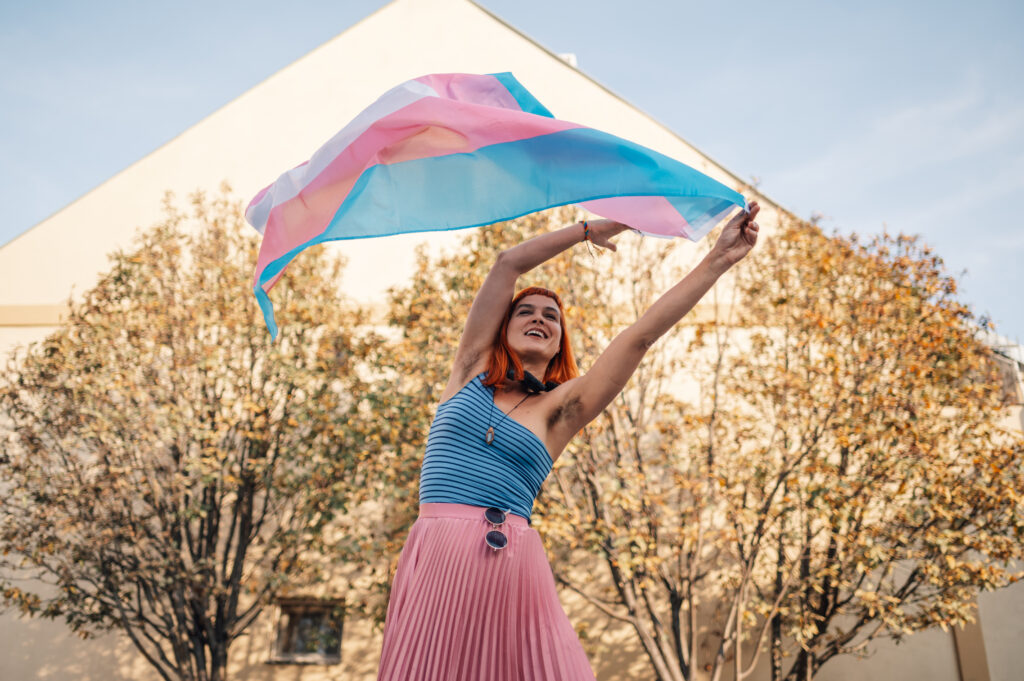 Mujer trans sonriendo con la bandera transgender al aire libre, representando la libertad económica de las creadoras trans en OnlyFans
